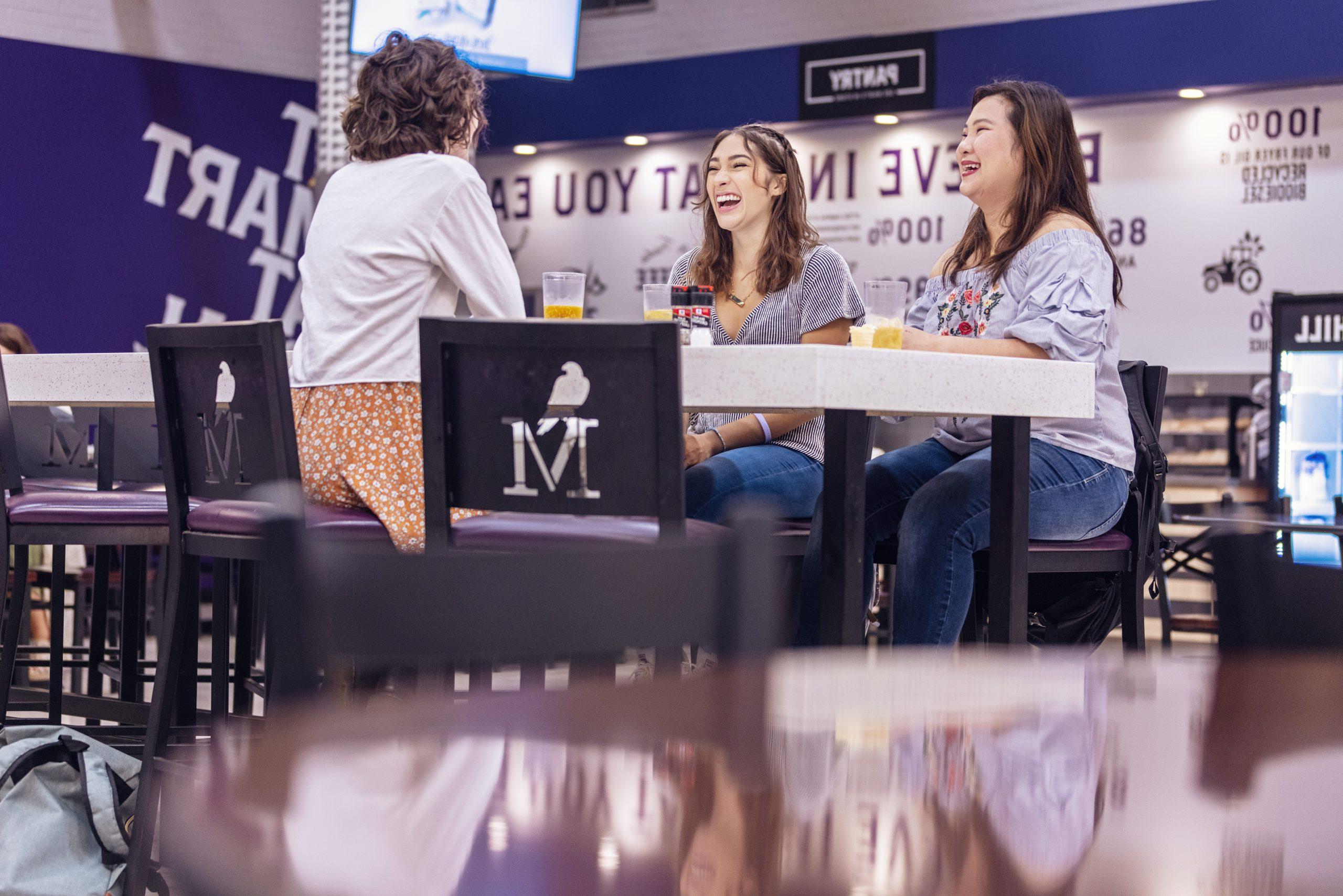 澳门在线赌城娱乐 students smile as they chat while sitting at a table in Anna Irvin Hall.